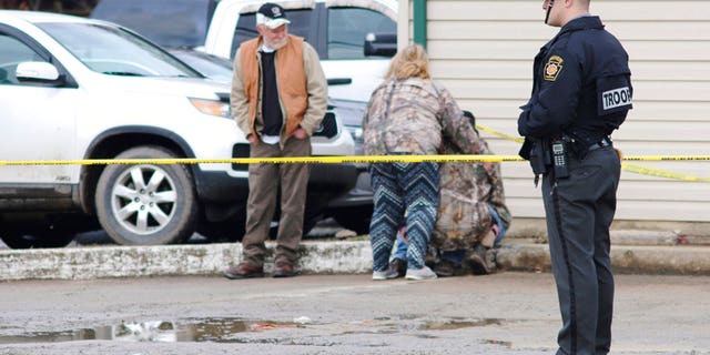 An officer stands guard as people comfort each other near the scene of a fatal shooting at a car wash in Melcroft, Pa., Sunday, Jan. 28, 2018.