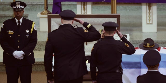 Two officers salute Chicago police Commander Paul Bauer before his funeral mass at Nativity of Our Lord Roman Catholic Church on Saturday in Chicago.
