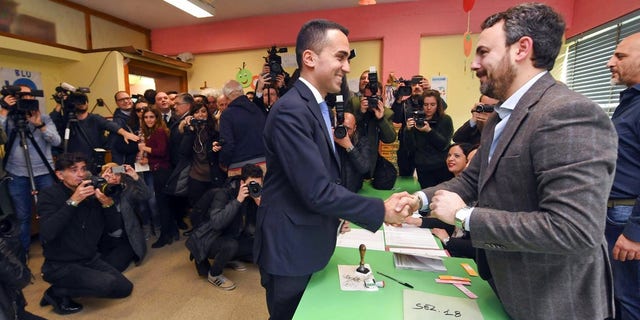 Five-Star movement's candidate premier Luigi Di Maio shakes hands with a polling clerk, right, as he votes in Pomigliano d'Arco, near Naples, Italy.