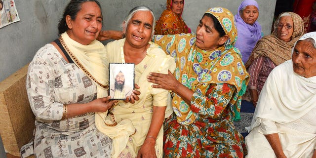 Relatives mourn holding a portrait of Gurcharan Singh, one of the 38 Indian workers whose bodies were found buried northwest of Mosul, in Jalal Usma village in the northern Indian state of Punjab, Tuesday, March 20, 2018. Iraqi authorities have found the bodies of 38 Indian workers abducted when Islamic State militants overran the northern city of Mosul more than three years ago, officials said Tuesday. (AP Photo/Prabhjot Gill)