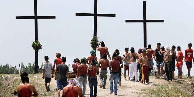 Filipino hooded penitents walk towards crosses during Good Friday rituals to atone for sins.