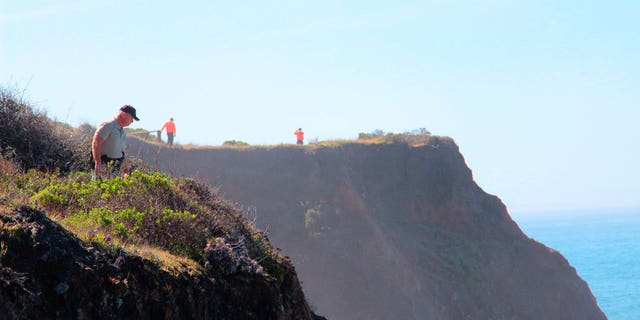 Deputy Bill Holcomb looks down a cliff near the site where the Harts fatally plunged into the rocky Pacific Ocean below, March 29, 2018.
