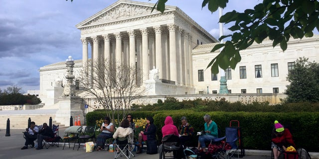 People wait in line outside the Supreme Court in Washington, to be in the gallery when the court hears arguments over President Trump's ban on travelers from several mostly Muslim countries.