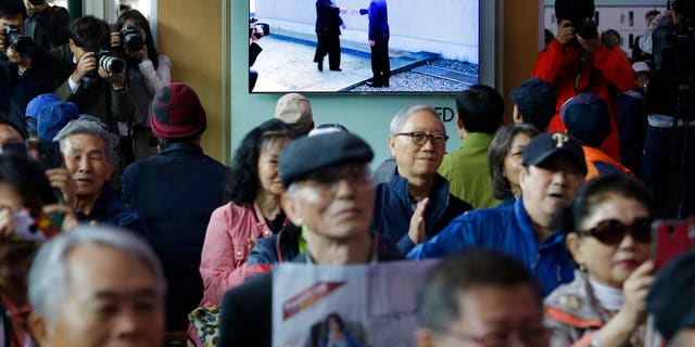 In this April 27, 2018 photo, People watch a TV screen showing the live broadcast of South Korean President Moon Jae-in, top right, meets with North Korean leader Kim Jong Un at the border village of Panmunjom during a news program at the Seoul Railway Station in Seoul, South Korea