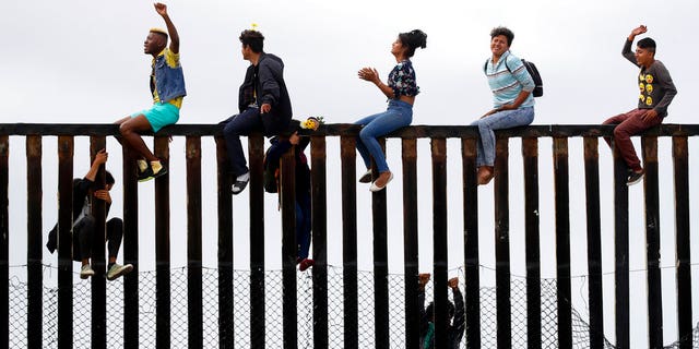 Central American migrants sit on top of the border wall on the beach in San Diego during a gathering of migrants living on both sides of the border, Sunday, April 29, 2018.
