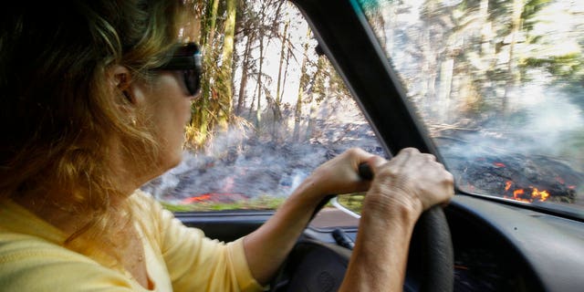 In this Sunday, May 6, 2018, photo, Leilani Estates resident Lucina Aquilina drives near lava on Luana Street in the Leilani Estates subdivision, in Pahoa, Hawaii.