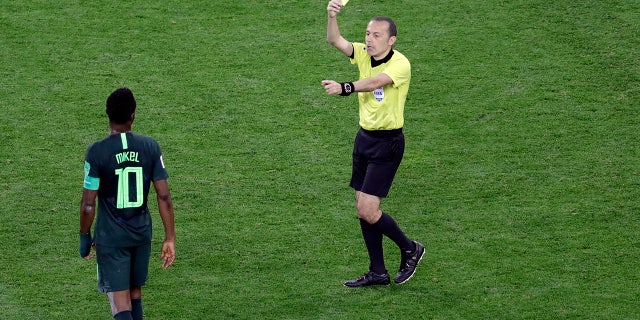 Referee Cuneyt Cakir shows a yellow card to Nigeria's John Obi Mikel during the group D match between Argentina and Nigeria.