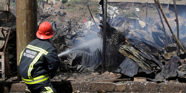 A fire fighter damps down charred debris after a fire swept through a marketplace in Nairobi, Kenya.