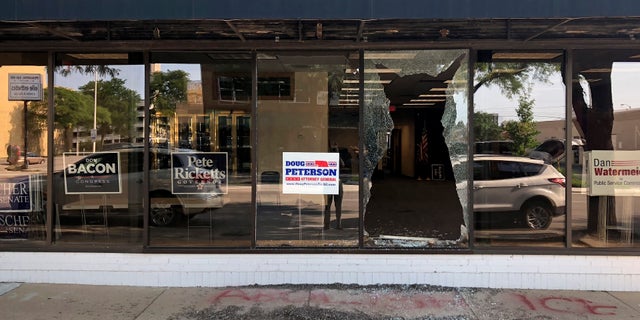 A broken window greets passers-by outside the Nebraska Republican Party's office in Lincoln, Neb., on Tuesday, July 3, 2018. Vandals threw a brick through the window overnight and scrawled the words "Abolish ICE" on the sidewalk below it.