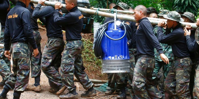 Soldiers carry a pump to help drain the rising flood water in a cave where 12 boys and their soccer coach have been trapped since June 23