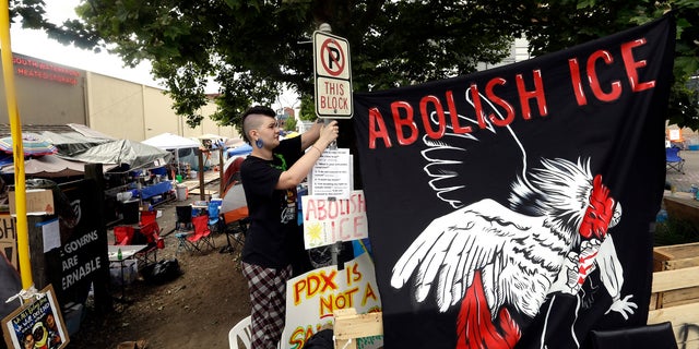 A woman hangs a sign at a protest camp on property outside the U.S. Immigration and Customs Enforcement office in Portland, Oregon.