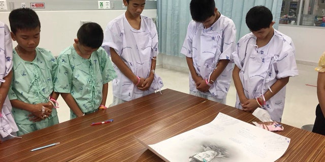 Some of the rescued soccer team members bowing their heads respectfully in front of a sketch of the Thai Navy SEAL diver who died while trying to rescue them.