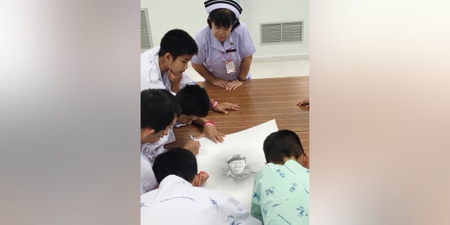 In this photo released by In this photo released by Thailand's Ministry of Health and the Chiang Rai Prachanukroh Hospital, some of the rescued soccer team members autographs and write notes on a sketch of the Thai Navy SEAL diver who died while trying to rescue them.