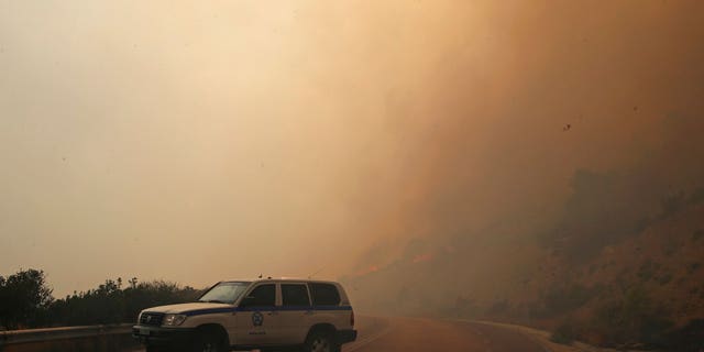 Smoke fills the sky as members of the emergency services block a road near Kineta, west of Athens, Monday, July 23, 2018.