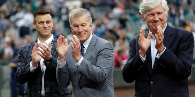 Seattle Mariners general manager Jerry Dipoto, left, president Kevin Mather, center, and majority owner John Stanton applaud during a presentation before a baseball game against the Detroit Tigers in Seattle, May 18, 2018.