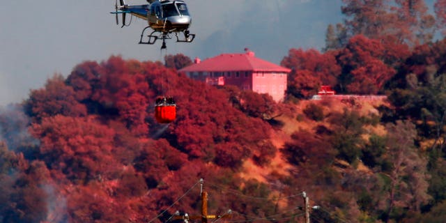 A helicopter battling a fire on Mt. Diablo passes a home covered in fire retardant, Wednesday, July 25, 2018, above Marsh Creek Road east of Clayton, Calif.