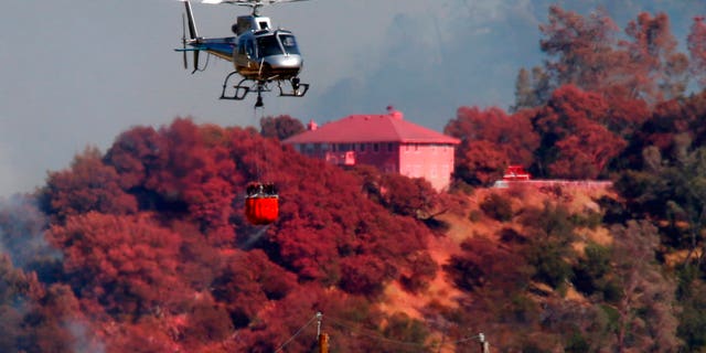 A helicopter battling a fire on Mt. Diablo passes a home covered in fire retardant, Wednesday, July 25, 2018, above Marsh Creek Road east of Clayton, Calif.