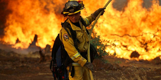 A firefighter makes a stand in front of an advancing wildfire as it approaches a residence Saturday, July 28, 2018, in Redding, California.