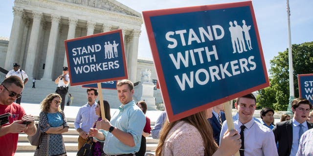 In this Monday, June 25, 2018, file photo, people gather at the Supreme Court awaiting a decision in an Illinois union dues case, Janus vs. AFSCME, in Washington.