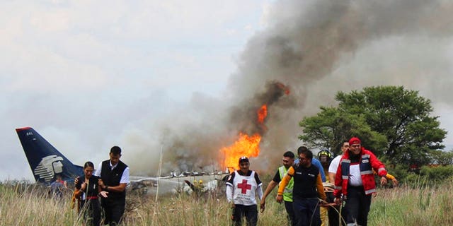 In this photo released by Red Cross Durango communications office, Red Cross workers and rescue workers carry an injured person on a stretcher, right, as airline workers, left, walk away from the site where an Aeromexico airliner crashed in a field near the airport in Durango, Mexico, Tuesday, July 31, 2018.