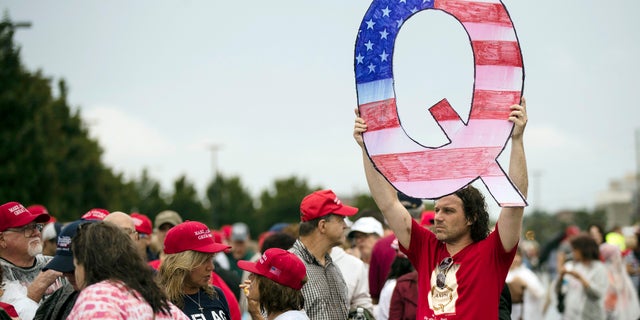 A man holds a 'Q' sign while waiting to enter a Pennsylvania rally with President Trump.