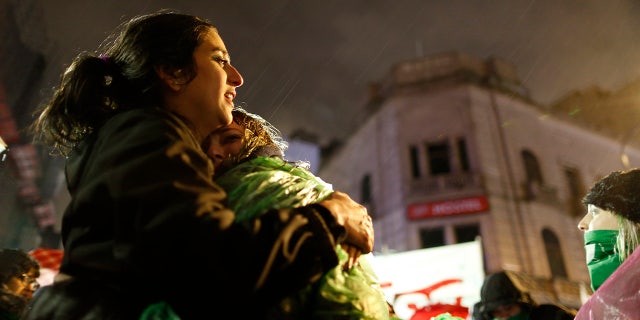 Tamara Deisel is embraced by her friend Florencia Buena as they stand under the rain outside Congress to show support for decriminalizing abortion as lawmakers debate the issue in Buenos Aires, Argentina.