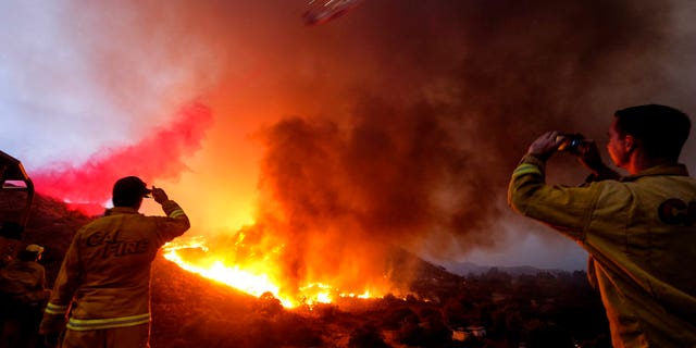 Members of Cal Fire take pictures while a plane drops water on the Holy Fire in the Cleveland National Forest in Lake Elsinore, Calif