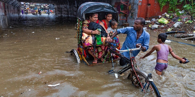An Indian rickshaw puller transporting two women and a child wades through a water logged street following heavy rains in Allahabad, India, Sunday, Aug. 12, 2018. India gets its monsoon rains from June to September. (AP Photo/Rajesh Kumar Singh)