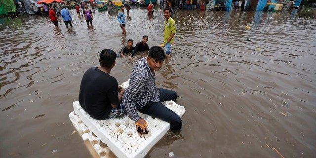 Indian men use thermocol sheets as a makeshift raft on a flooded road after heavy rainfall in Ahmadabad, India.