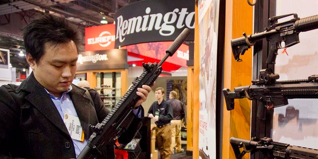 FILE- In this Jan. 15, 2013, file photo, accessories manufacturer Kevin Kao, of Irvine, Calif., examines a military grade Remington Adaptive Combat Rifle at the 35th annual SHOT Show in Las Vegas. A U.S. judge has struck down a nearly century-old California law that banned gun shops from advertising handguns on their premises. Judge Troy Nunley in Sacramento ruled Tuesday, Sept. 11, 2018, that the law violated the First Amendment. Nunley said the state failed to show that enforcing the law would prevent violence or suicides. The ruling came in a lawsuit filed in 2014 by several gun dealers who were fined by the state for handgun ads. The 1923 law banned any handgun ads at gun shops that were visible from outside the store. (AP Photo/Julie Jacobson, File)