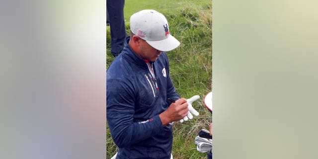 Koepka signs an autograph on his golf glove to a spectator he hit with his ball during his fourball match on the opening day of the 42nd Ryder Cup at Le Golf National in Saint-Quentin-en-Yvelines