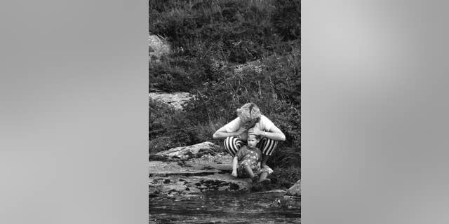 Princess Diana plays with Prince Harry by a stream.