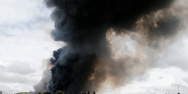 Four women walk with masks in front of billowing black smoke from a huge fire in Sesena, central Spain, Friday, May 13, 2016. A massive fire is raging at a sprawling tire dump in a town near Madrid, sending a spectacular cloud of thick black smoke into the air that's visible for at least 30 kilometers (20 miles). Ten teams of firefighters are trying to put out the blaze at the tire dump in the town of Sesena, still raging more than 10 hours after it started. (AP Photo/Paul White)