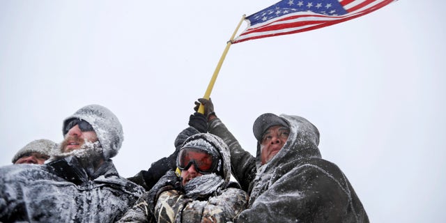 Military veterans huddle together to hold an American flag against strong winds during a march in Cannon Ball, N.D., on Monday.