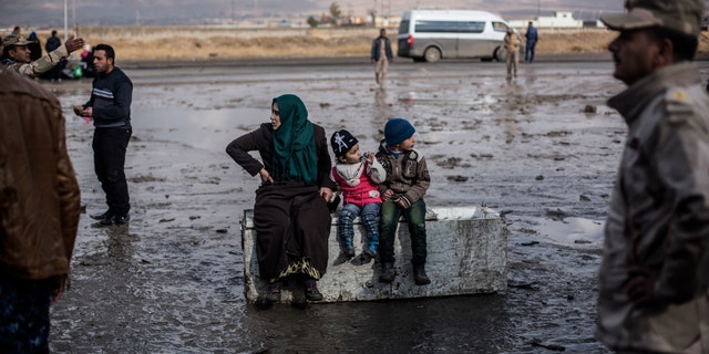 An Iraqi woman displaced from Mosul and her 2 children sit on top of an old refrigerator at a gathering point for displaced people, in Bartella, around 19 miles from Mosul.
