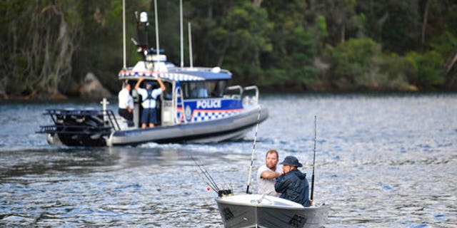 Fishermen guide their boat past a police vessel at the scene where a seaplane crashed into the Hawkesbury River.