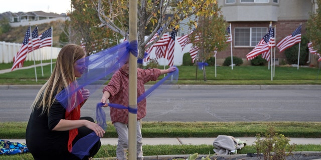 Kimberlee Jensen places a blue ribbon around a flag pole with her son last week across the street from Officer Cody Brotherson's home.