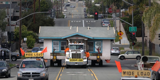 In this photo taken Monday, March 28, 2016, workers oversee the hauling of a small home in Hillcrest, Calif., as it left the plot of land on the corner of Vermont Street and is moving east along Howard Avenue. The home, built in 1925, was being moved to a storage yard in Otay Mesa, Calif., before finally being relocated to a new lot in Chula Vista, Calif. The owner, Anne Wilson, had lived in the 800-square-foot stucco home for 23 years, plans to build a new three-story home on the lot. (Peggy Peattie/The San Diego Union-Tribune via AP) NO SALES; MANDATORY CREDIT