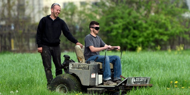 In this photo taken Wednesday May 11, 2016, Detroit Mower Gang members Gage Vaneckoute, left, of Bellville, Mich., laughs at the path his brother Chase has taken during a blindfolded mower contest at Hammerberg Field on Detroit's west side. The volunteers helping to maintain Detroit parks and playgrounds took a crack at mowing grass while blindfolded as part of a friendly competition. (Steve Perez/Detroit News via AP) DETROIT FREE PRESS OUT; HUFFINGTON POST OUT; MANDATORY CREDIT