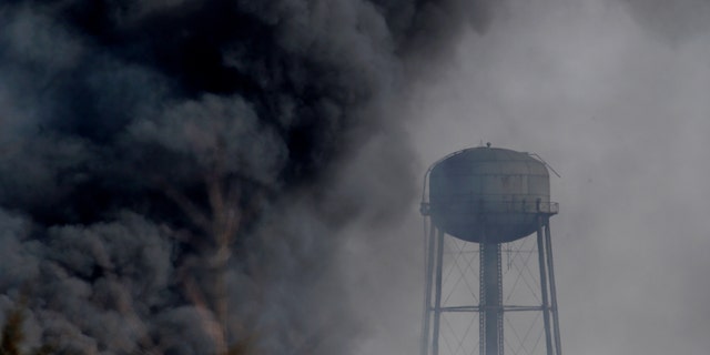 Smoke rises near a water tower at the site of a large warehouse fire a day after flames engulfed the facility, Friday, Feb. 12, 2016, in Hillsborough, N.J. Firefighters have contained the massive  fire and officials said the blaze didn't pose an imminent public health threat. Fire officials say plastic pellets were being stored in most of the complex, and environmental officials have been testing air quality. (AP Photo/Julio Cortez)