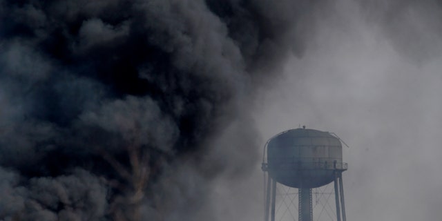 Smoke rises near a water tower at the site of a large warehouse fire a day after flames engulfed the facility, Friday, Feb. 12, 2016, in Hillsborough, N.J. Firefighters have contained the massive fire and officials said the blaze didn't pose an imminent public health threat. Fire officials say plastic pellets were being stored in most of the complex, and environmental officials have been testing air quality. (AP Photo/Julio Cortez)