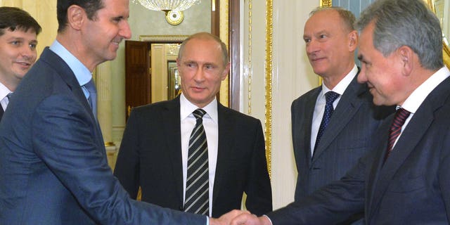 Assad, second left, shakes hand with Shoigu as Russian President Vladimir Putin, center, looks on, in October 2015.