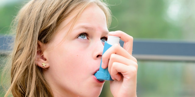 Girl having asthma using the asthma inhaler for being healthy - shallow depth of field - asthma allergy concept
