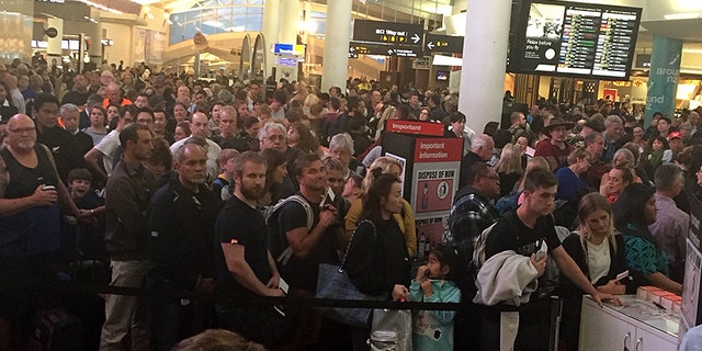 Crowds of passengers await the re-opening of airport security after a woman took a knife into the Auckland Airport's international terminal.