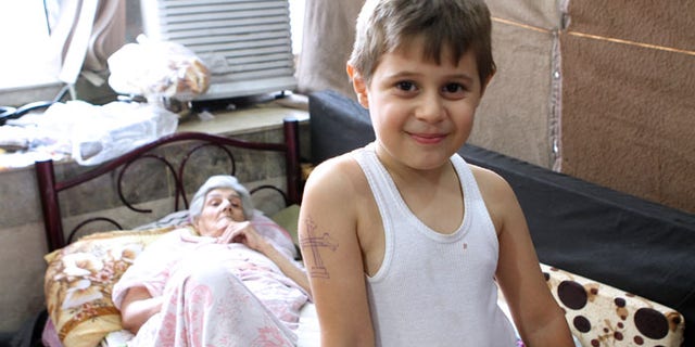 Aws, a 10-year-old Iraqi Christian boy, has spent much of his young life fleeing jihadists. Munira Aziz, 74,pictured behind him, considers herself fortunate to have escaped ISIS. (Benjamin Hall)