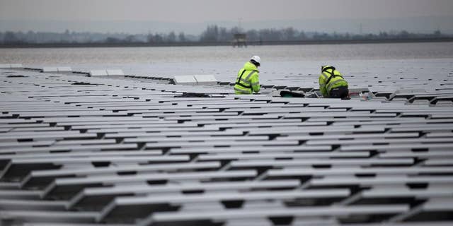 FILE - This is a  Monday, March 21, 2016 file photo of contractors continue work on Europe's biggest floating solar panel array as it nears completion on the Queen Elizabeth II Reservoir near Walton-on-Thames in south west London.  Data published Tuesday June 21, 2016 by the European Environment Agency show that Britain’s greenhouse gas emissions fell by 34.3 percent in 1990-2014, the biggest percentage drop in the EU except for eastern countries whose emissions fell sharply when communist-era heavy industries collapsed. (AP Photo/Matt Dunham, File)