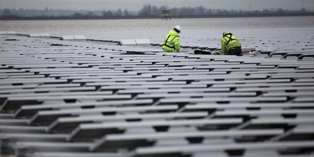 FILE - This is a Monday, March 21, 2016 file photo of contractors continue work on Europe's biggest floating solar panel array as it nears completion on the Queen Elizabeth II Reservoir near Walton-on-Thames in south west London. Data published Tuesday June 21, 2016 by the European Environment Agency show that Britain’s greenhouse gas emissions fell by 34.3 percent in 1990-2014, the biggest percentage drop in the EU except for eastern countries whose emissions fell sharply when communist-era heavy industries collapsed. (AP Photo/Matt Dunham, File)