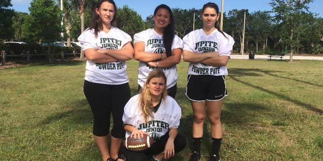 FILE - In this May 2, 2016, file photo, Jupiter High School powderpuff football players, from left, Caitlin Walsh, Megan Mendoza, Haley Osborne and Savannah Tardonia (in front with ball) pose for a group photo in Jupiter, Fla. Almost sacked for safety concerns after 50 years, the nation's last tackle powderpuff football game will now be played. Students and parents from Florida's Jupiter High School persuaded the town to sponsor the all-girl game after the principal cancelled, fearing girls would be injured. (AP Photo/Terry Spencer, File)