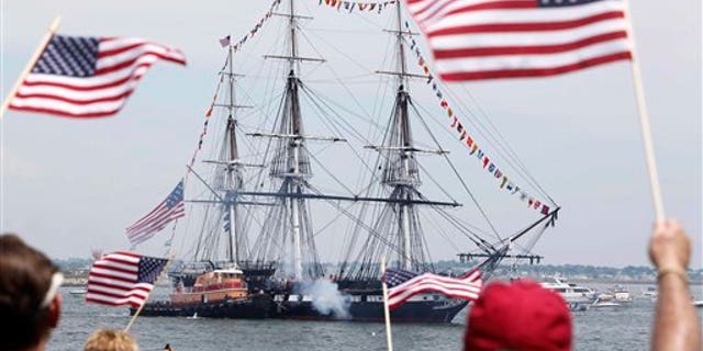 Pada tanggal 4 Juli, penonton mengibarkan bendera saat Konstitusi USS menembakkan meriamnya dari Castle Island pada pergantian tahunan 4 Juli di Pelabuhan Boston.