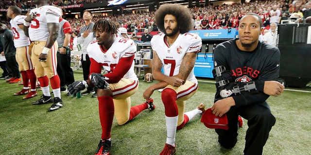 El mariscal de campo de los 49ers, Colin Kaepernick (centro), se arrodilla durante un partido de la NFL para protestar contra la brutalidad policial.